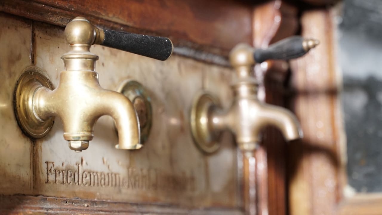 Zwei alte Messing-Zapfhähne mit schwarzen Griffen am historischen Schanktisch des Gasthofs